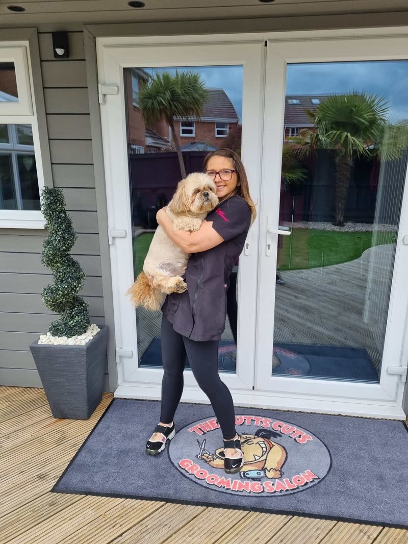 The groomer at the salon's glass entrance doors holding a freshly groomed small dog